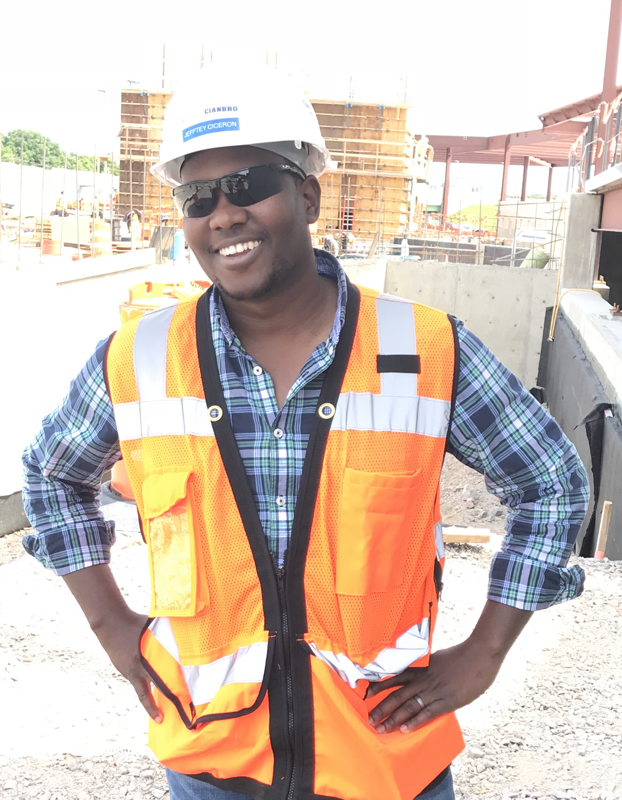 Construction worker with hands on hips, wearing on orange vest and smiling.