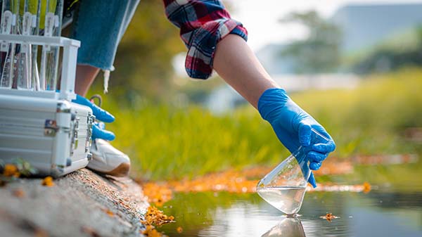 person on water bank scooping water into beaker